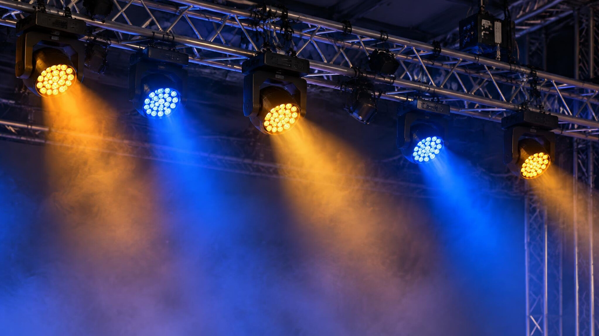 Overhead lighting truss with multiple fixtures glowing above a stage